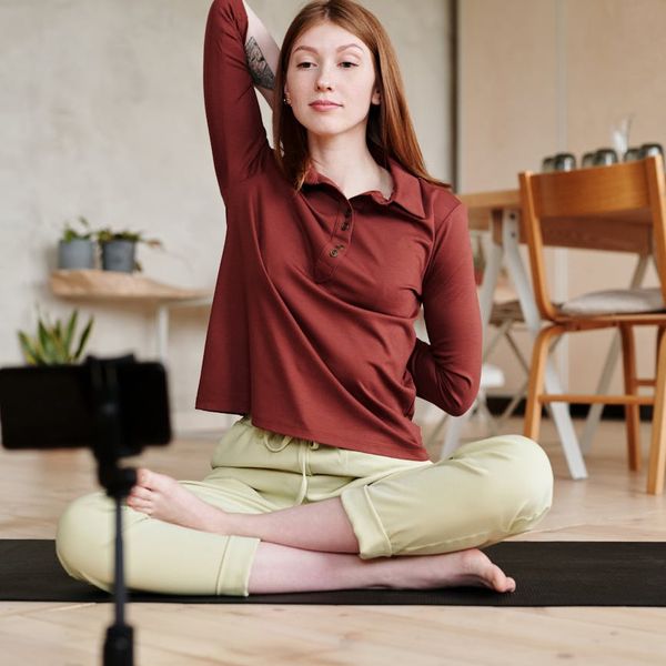 Smiling woman meditating on a yoga mat near a large window.